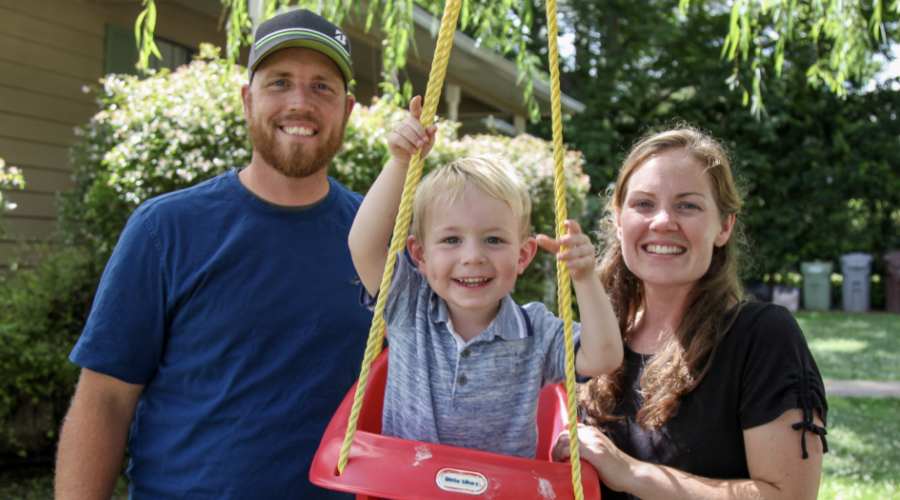 A family pushing their son on a swing.