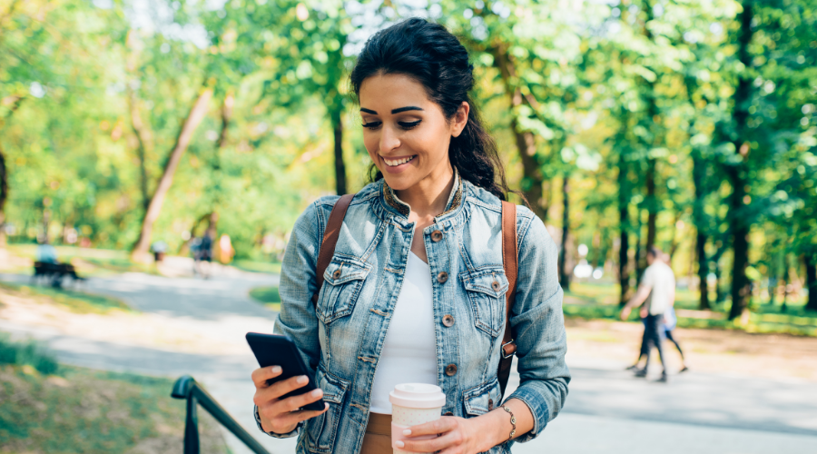 A woman walks through the park, checking her phone to see how much her credit score has improved with the help of Civic's Credit Builder Loan.