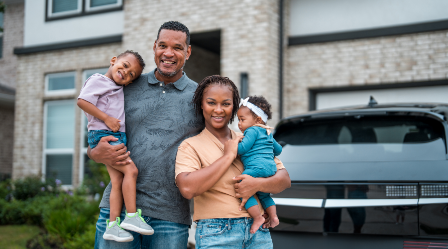 A family standing in their driveway in front of their home and parked car.