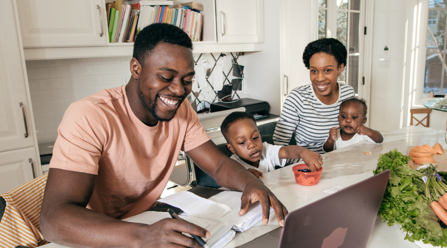 A dad, mom, and their two young children sit at the dining table as dad applies for a Civic Personal Line of Credit Loan.