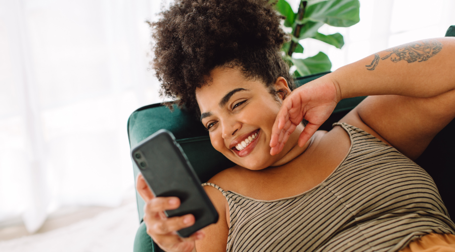 A woman relaxes on the sofa, checking her Steady Save Savings Account through the Civic mobile app.