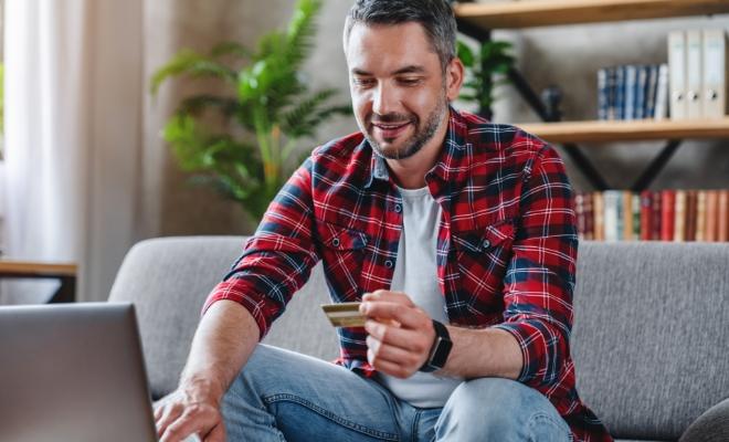Happy middle aged man holding Civic Classic Credit Card and using laptop at home for shopping.