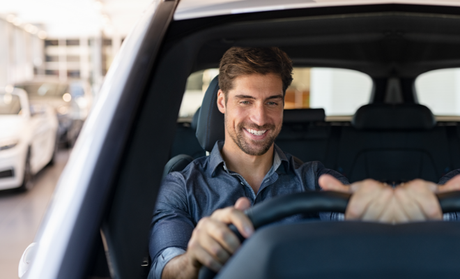 Smiling man sitting behind the wheel of a car, symbolizing ease and satisfaction with a Civic used auto loan.