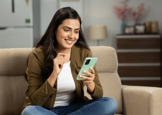 A woman in her living room on her mobile phone is excited she could qualify for a special mortgage program to buy a house.