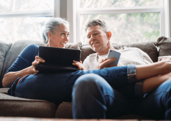 An older couple on a comfy sofa apply for a fixed-rate mortgage loan to refinance their home using their mobile devices.