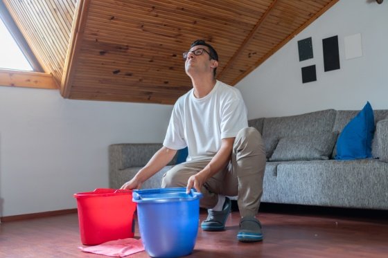 Man holding out two buckets trying to catch water leak