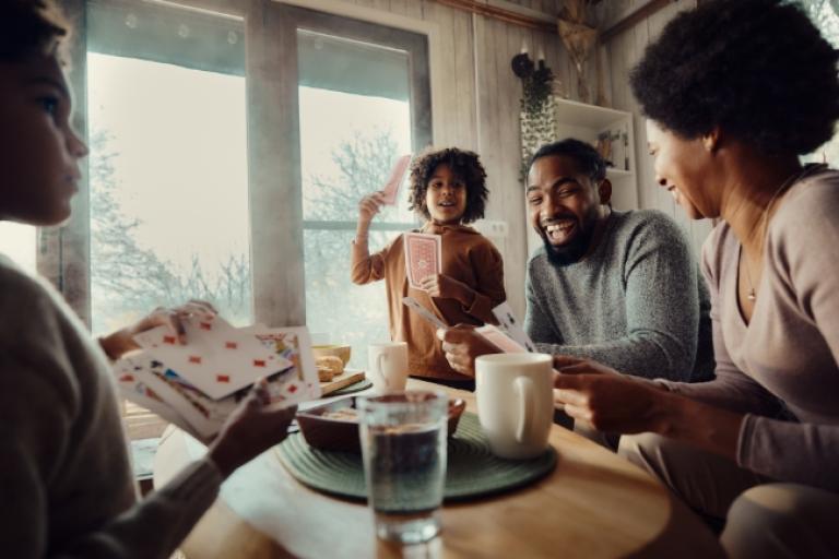 Happy African American family playing cards at home after a day of holiday shopping with the Civic Classic Credit Card.