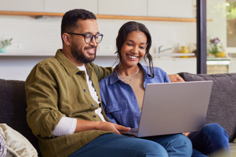 A couple sitting comfortably on their living room couch, setting up Bill Pay.