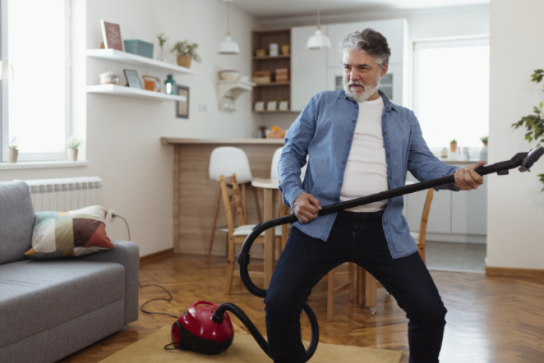 An older gentleman pauses from cleaning to play the vacuum like a guitar, all while knowing his Civic Health Savings Account has him covered for any medical expenses.