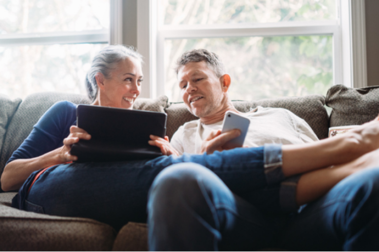 Couple lounging on the couch, on their devices, discussing their Civic Savings Account.