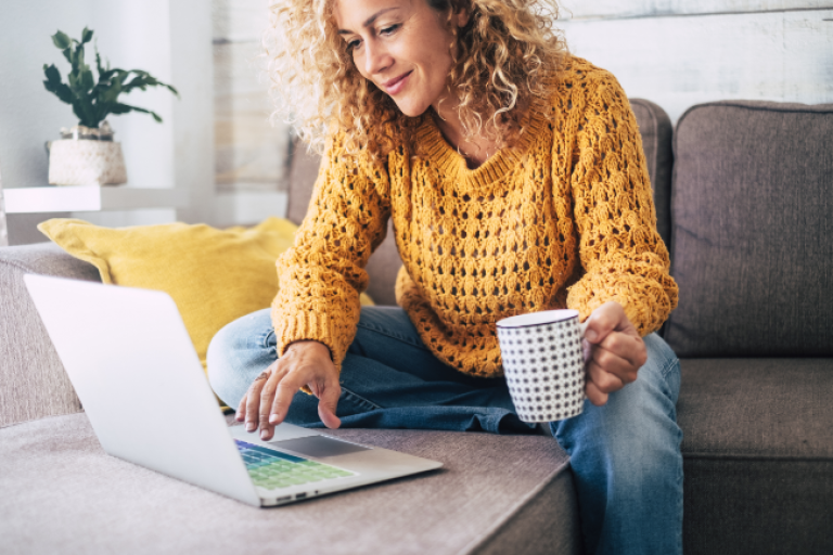 A woman sitting on her sofa with her laptop on the coffee table, opening a Civic Steady Save Savings Account.