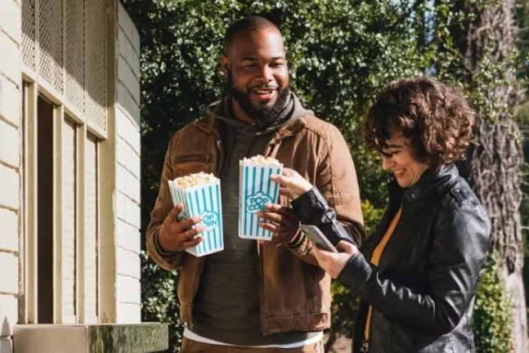 A group of friends heading into the movies, with one sending money via Zelle to repay for the movie tickets and popcorn.