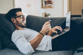 Man laying on couch using at credit card